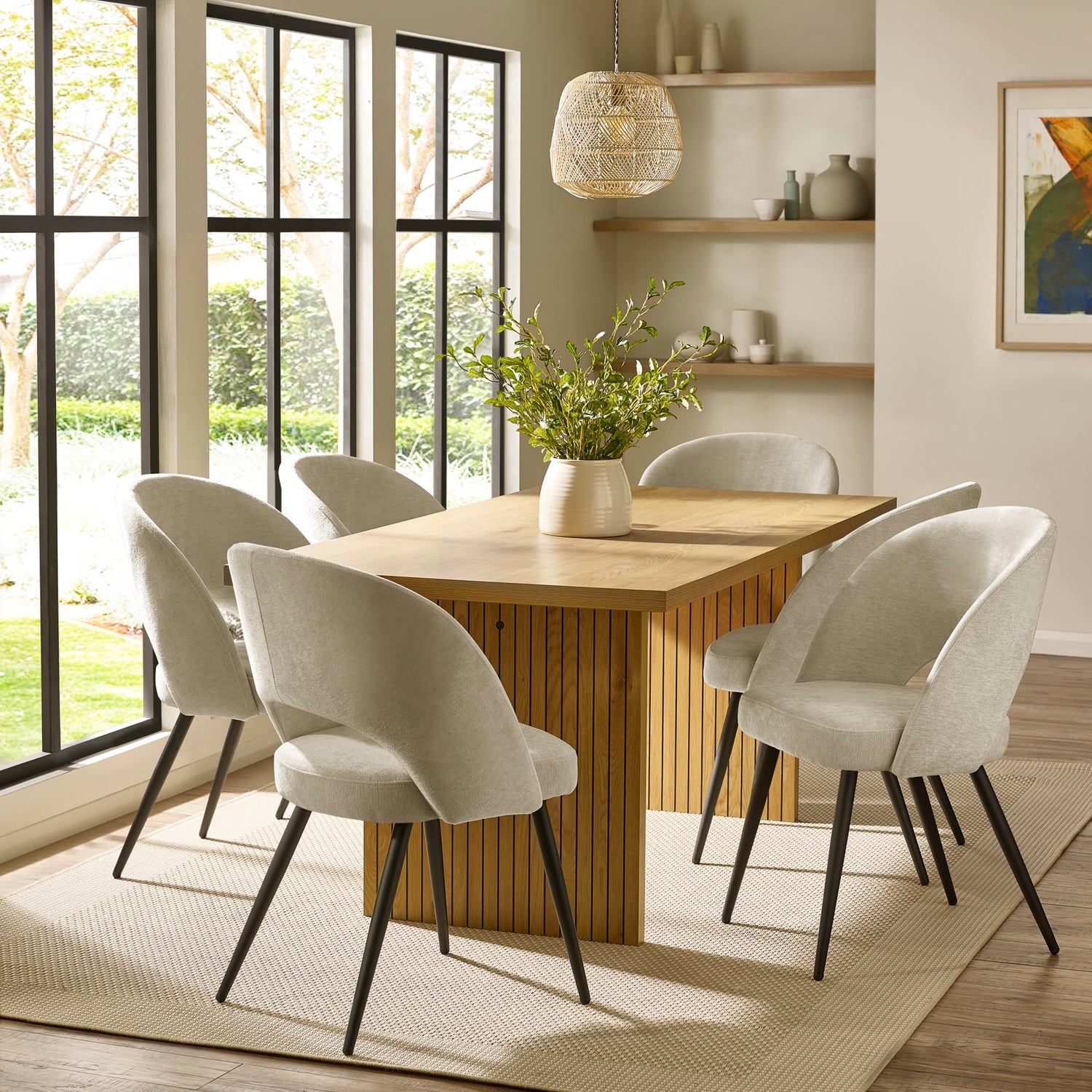 Dining room with wooden table and white chairs near large windows.