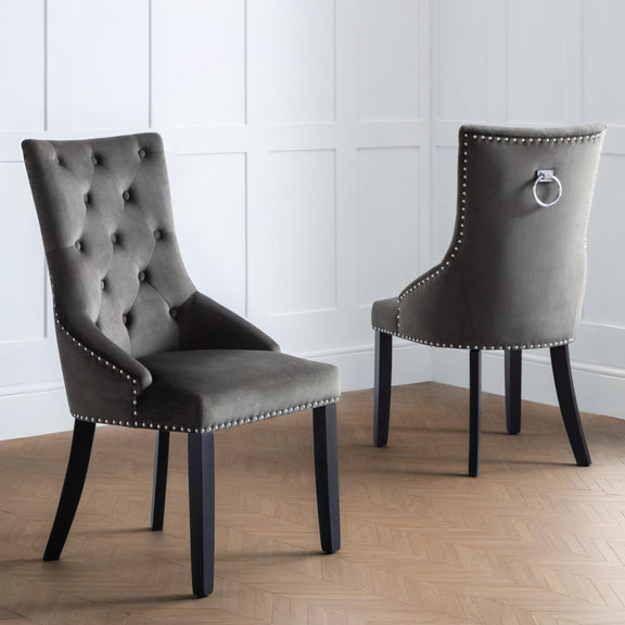 Two gray upholstered chairs with nailhead trim on a wooden floor.