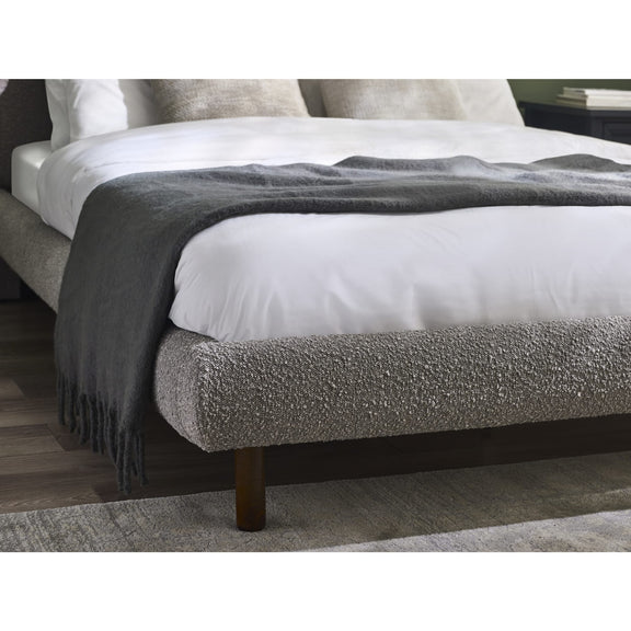 Gray upholstered bed with white mattress and gray blanket on a wooden floor.