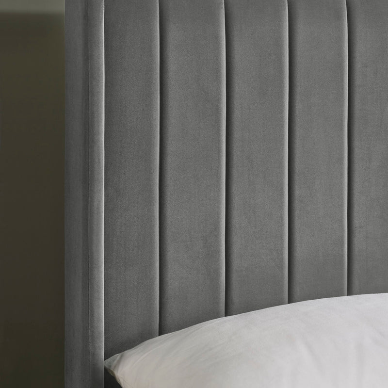 Gray upholstered headboard with a pillow on a bed against a dark background