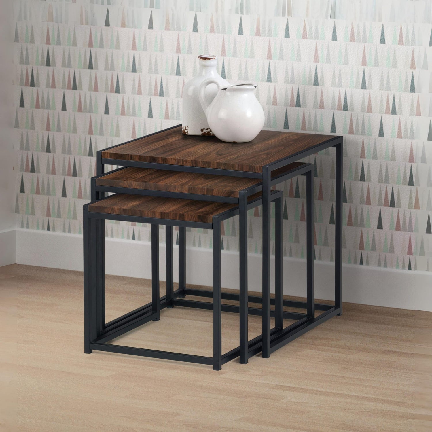 Set of three nesting tables with wooden tops and black metal frames against a patterned wall.