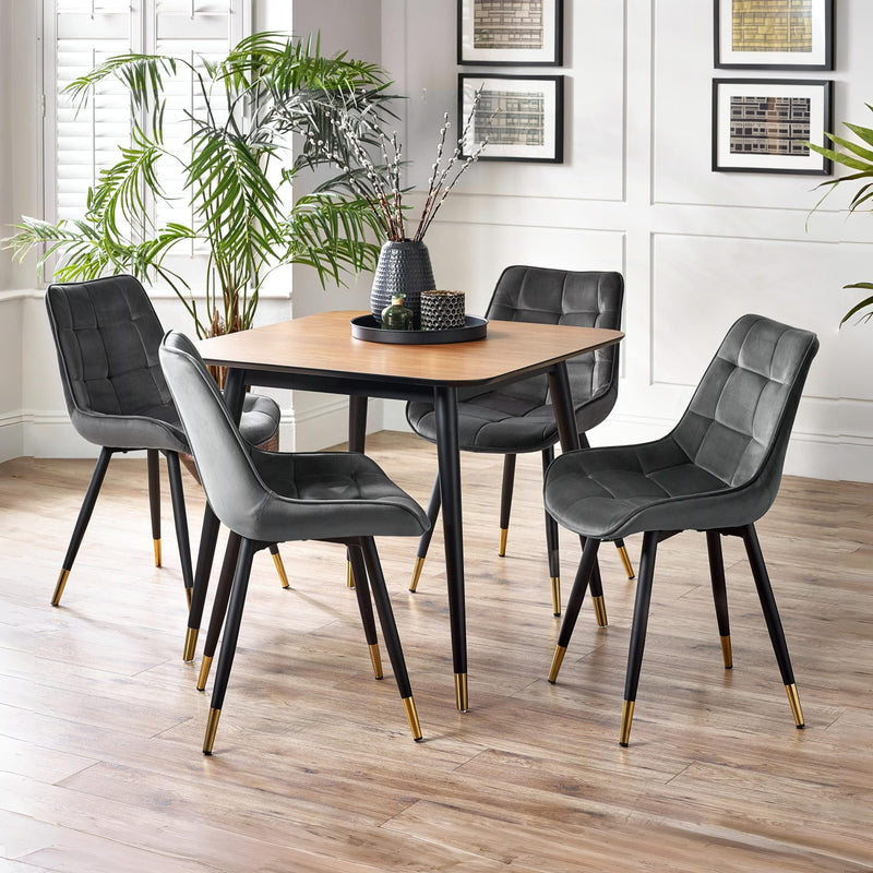 Dining table set with four gray chairs in a room with plants and framed pictures.