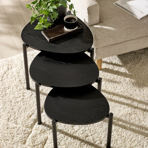 Black nesting tables with a plant and coffee cup on a white carpeted floor.