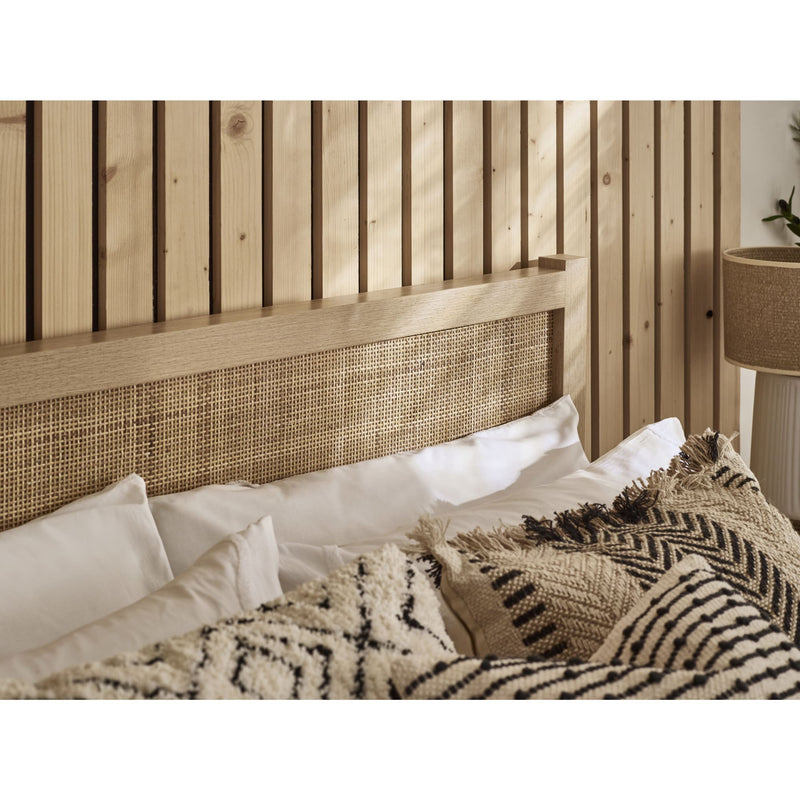 Bed with woven headboard and textured bedding against a wooden wall.