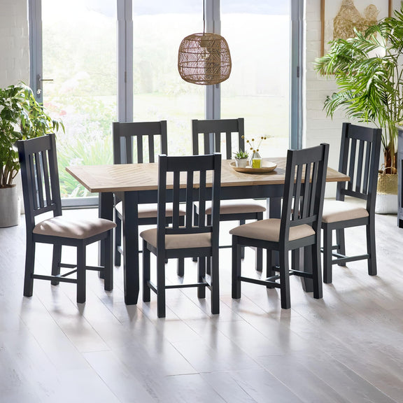 Dining table set with black chairs and beige cushions in a bright room with plants.