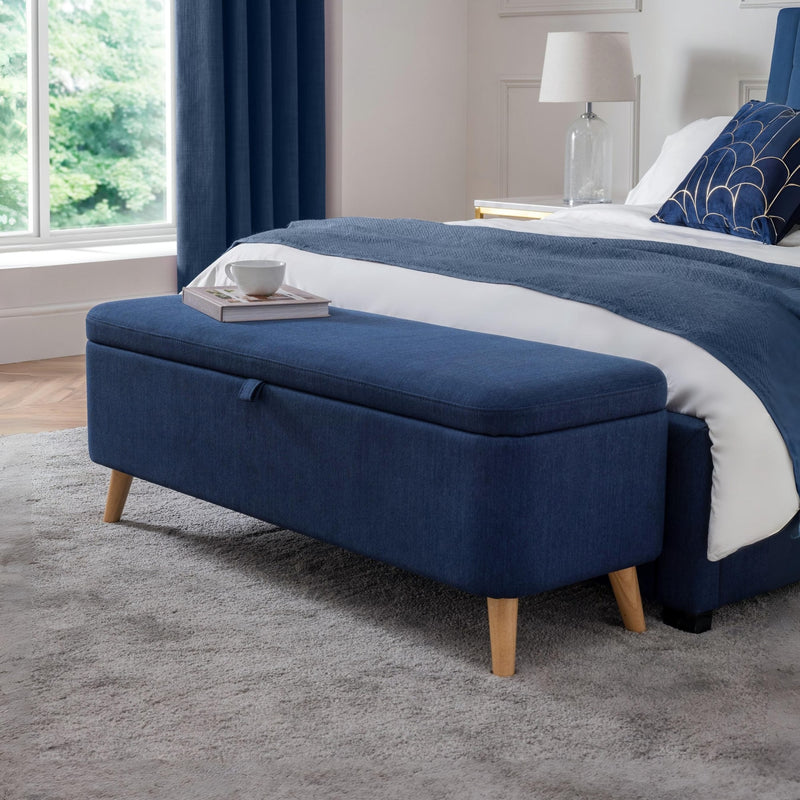 Blue ottoman with wooden legs in a bedroom setting.