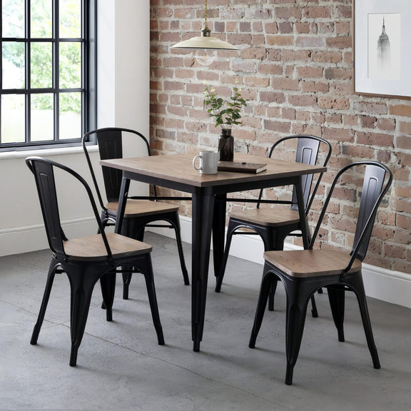 Dining area with a square table and black metal chairs against a brick wall.