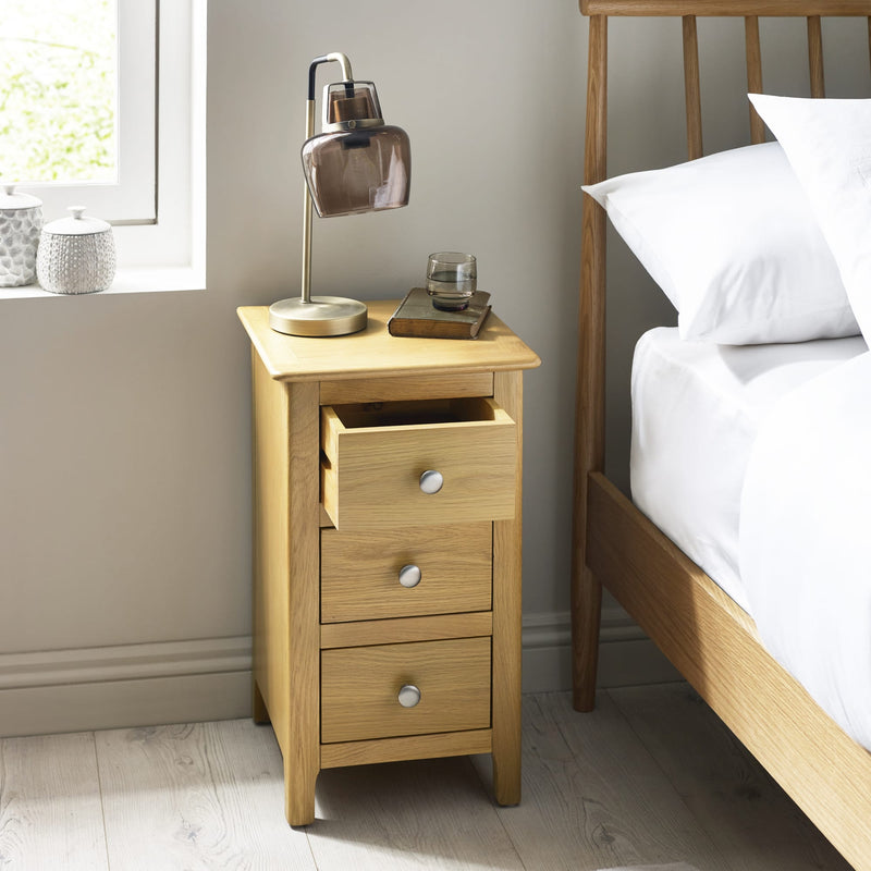 Wooden nightstand with two drawers next to a bed in a bedroom setting.