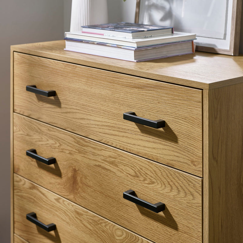 Wooden dresser with four drawers and black handles, with books on top.