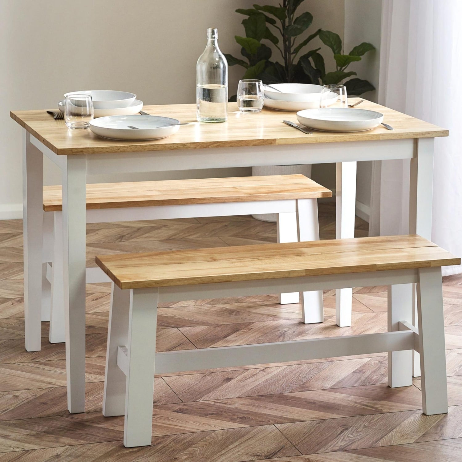 Dining table with benches on a wooden floor, set with plates and glasses.
