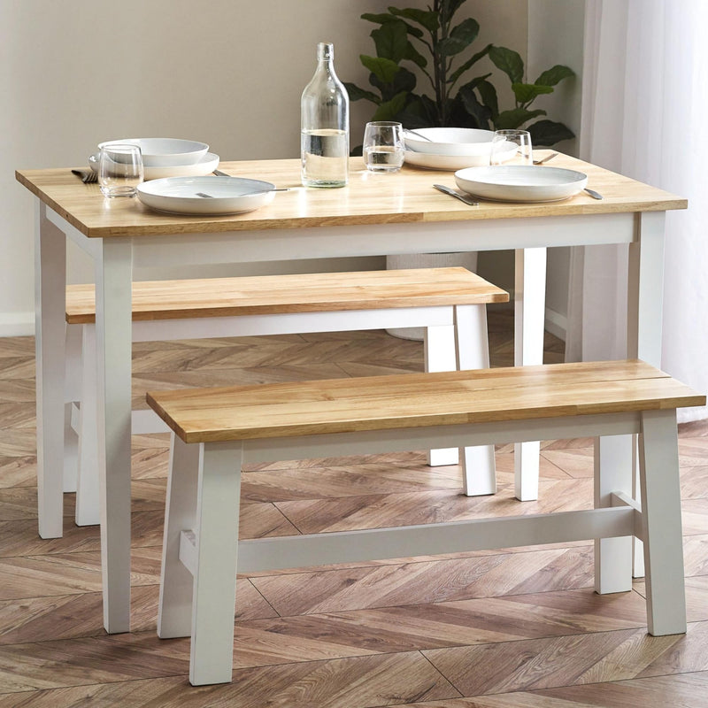 Dining table with benches on a wooden floor, set with plates and glasses.