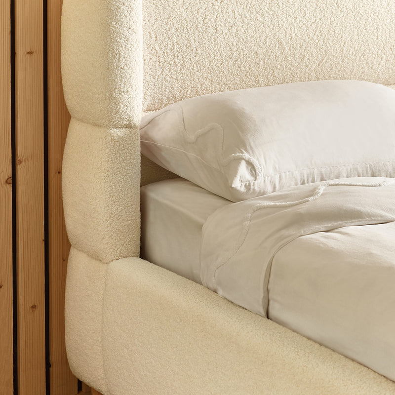 Close-up of a textured headboard and bedding with a pillow.