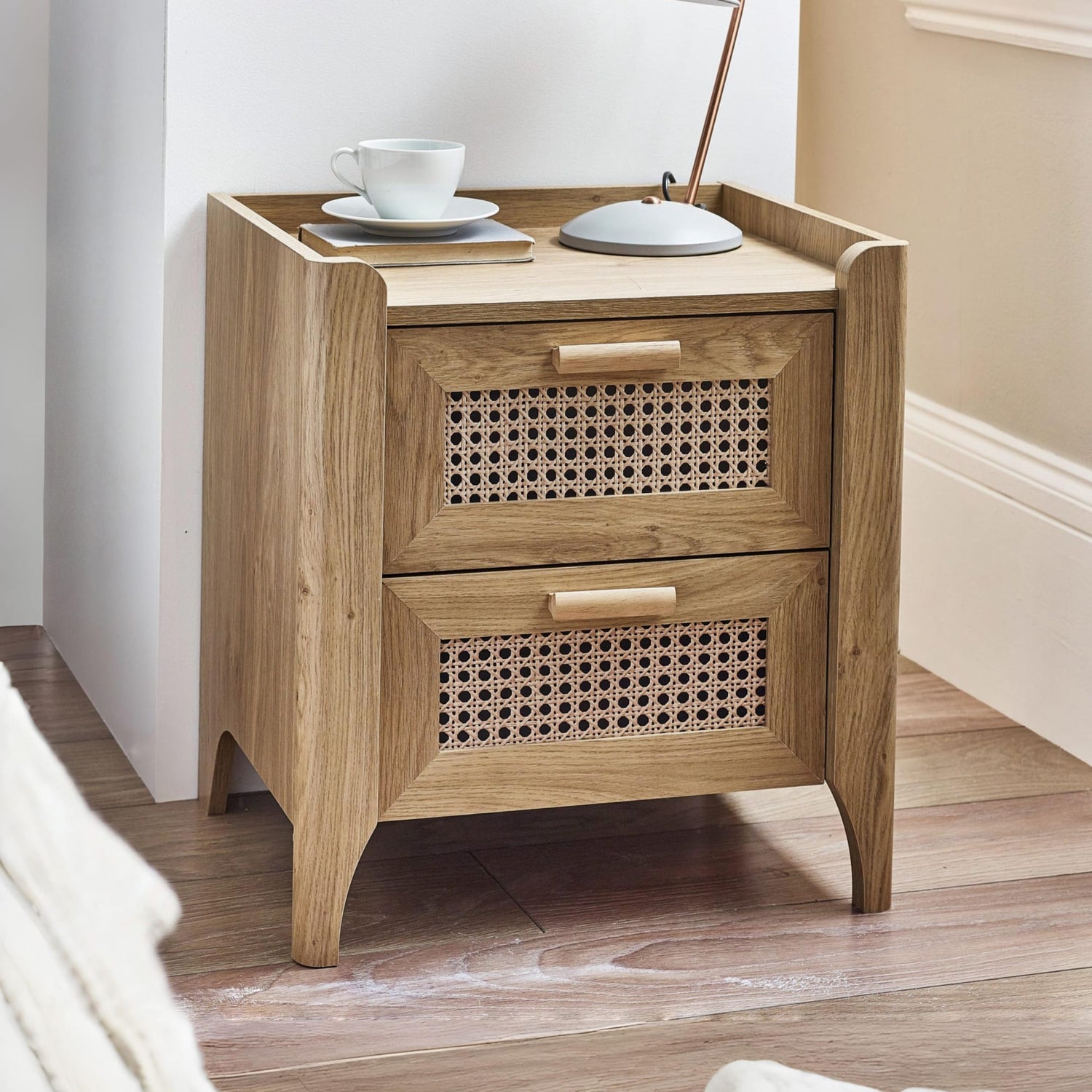 Oak effect wooden bedside table with two woven rattan drawers beside bed