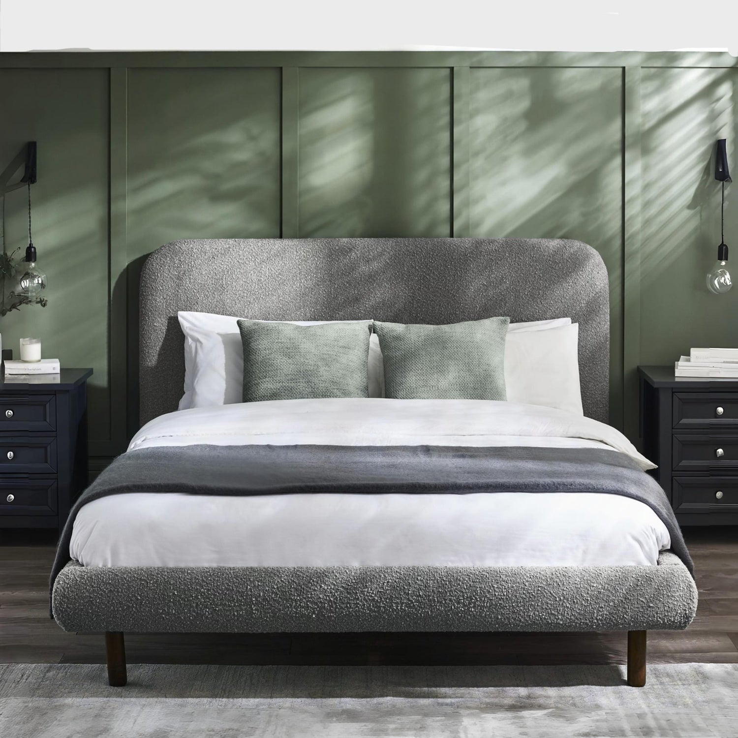 Gray upholstered bed with white bedding in a bedroom setting with green walls.