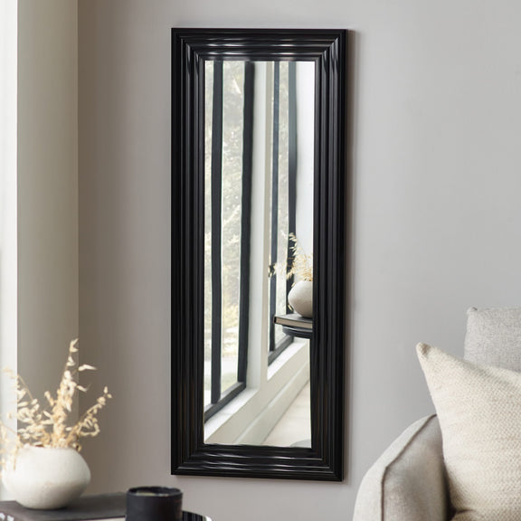 Black-framed mirror on a gray wall with decorative elements.