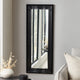 Black-framed mirror on a gray wall with decorative elements.