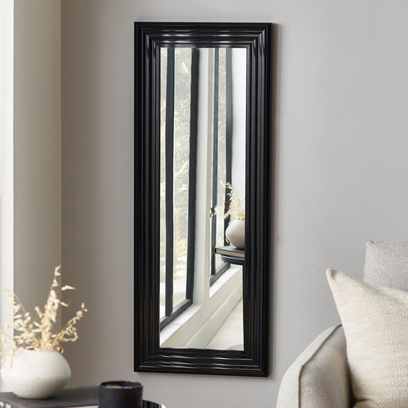 Black-framed mirror on a gray wall with decorative elements.