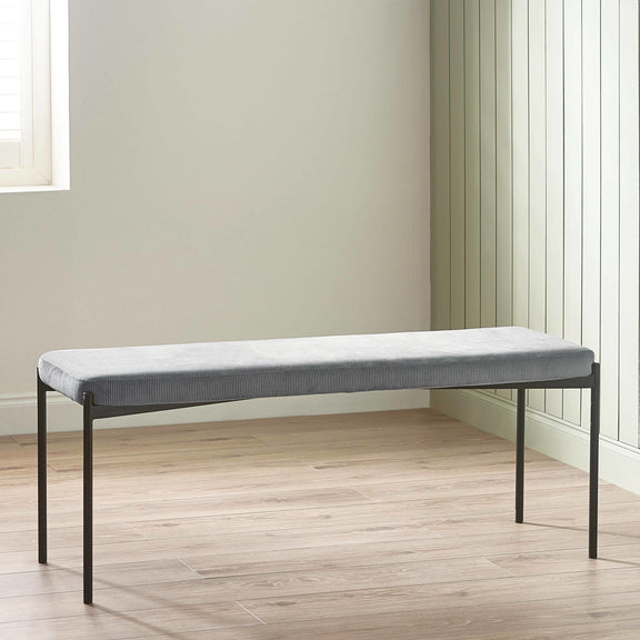 Gray upholstered bench with black metal frame on a wooden floor.