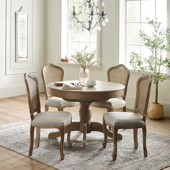 Round wooden dining table with four chairs in a well-lit room with large windows.