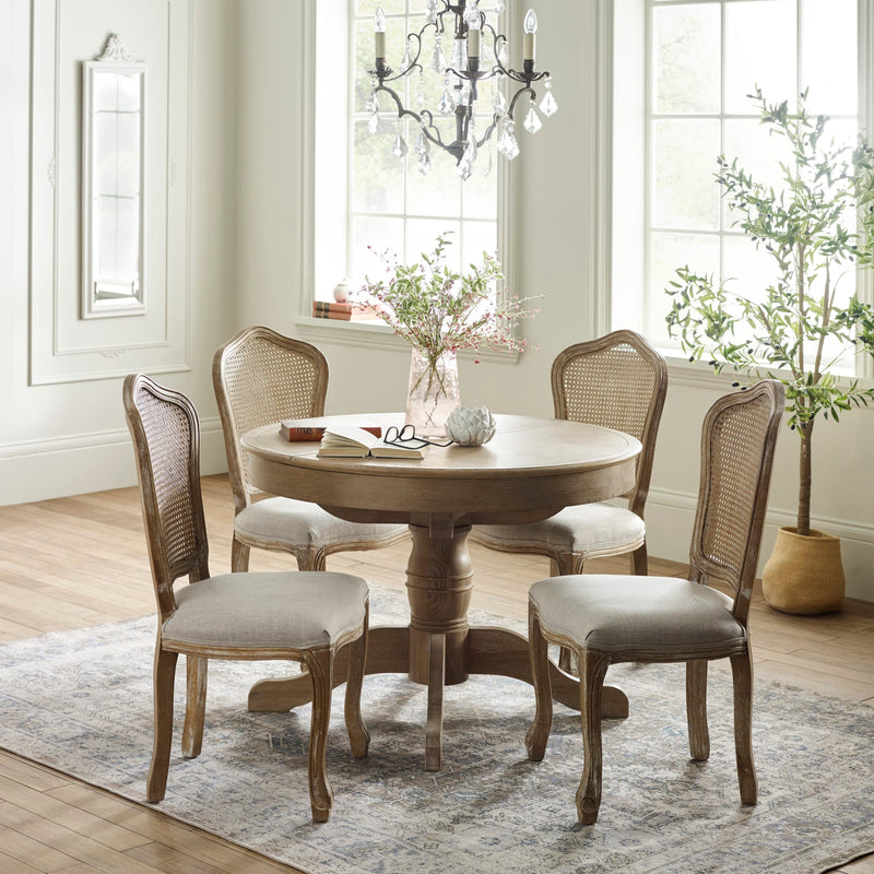 Round wooden dining table with four chairs in a well-lit room with large windows.