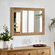 Wooden dresser with mirror, flowers, and glasses on a white wall.