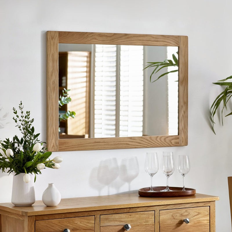 Wooden dresser with mirror, flowers, and glasses on a white wall.