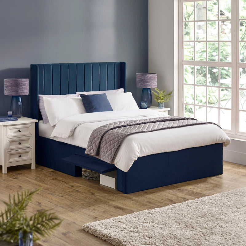 Navy bed with white bedding in a bedroom setting with lamps and decor.
