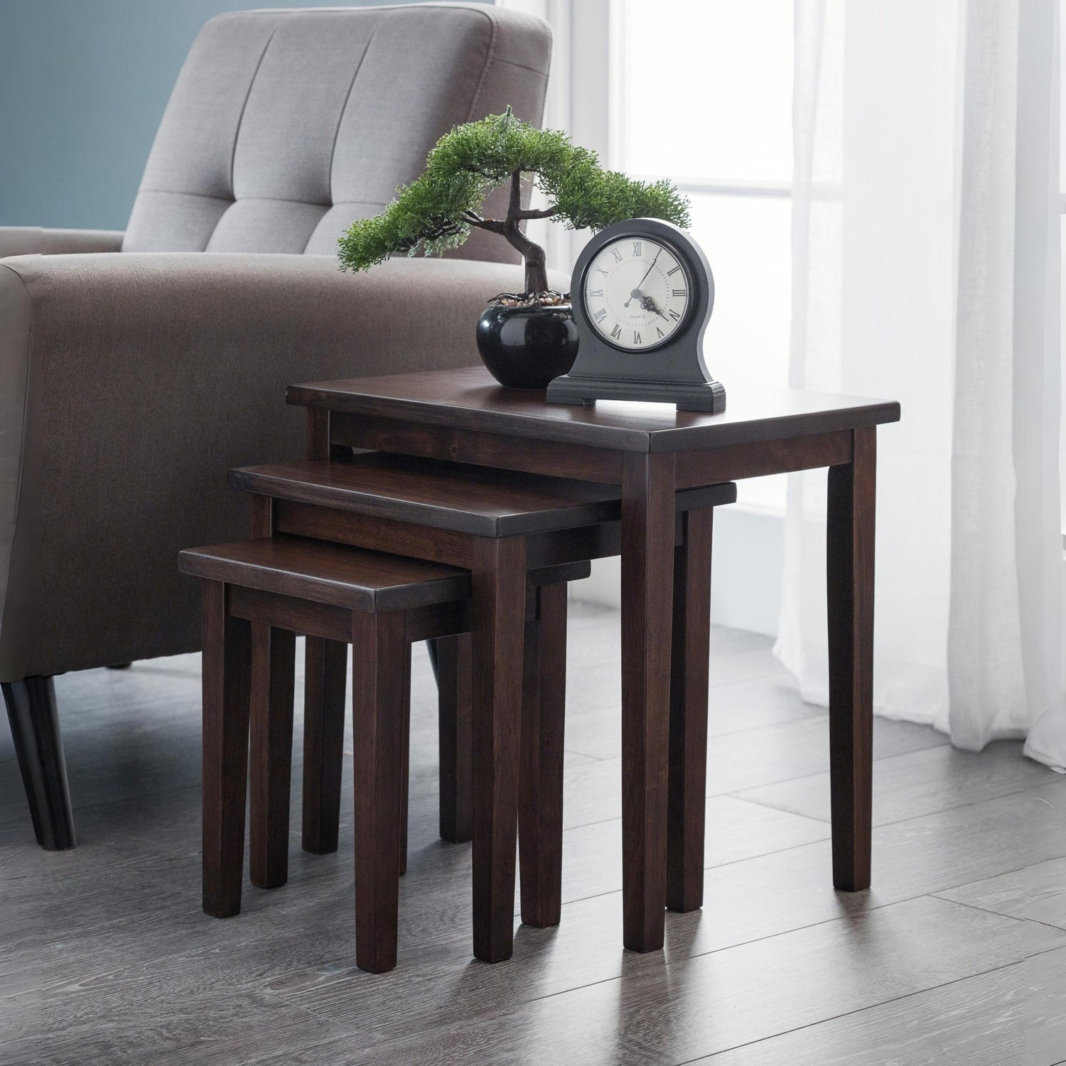 Set of four dark wood nesting tables in a living room setting with a chair and decorative items.
