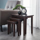 Set of four dark wood nesting tables in a living room setting with a chair and decorative items.