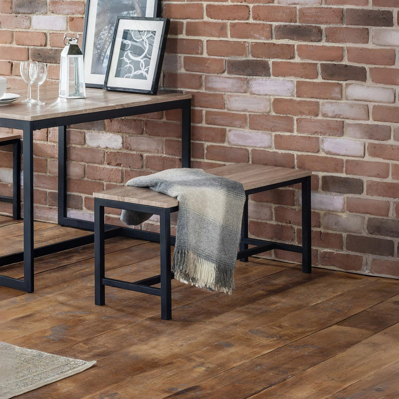 Wooden bench with a blanket against a brick wall in a room with wooden flooring.