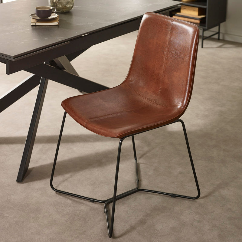 Brown leather chair with black metal legs in front of a wooden table.