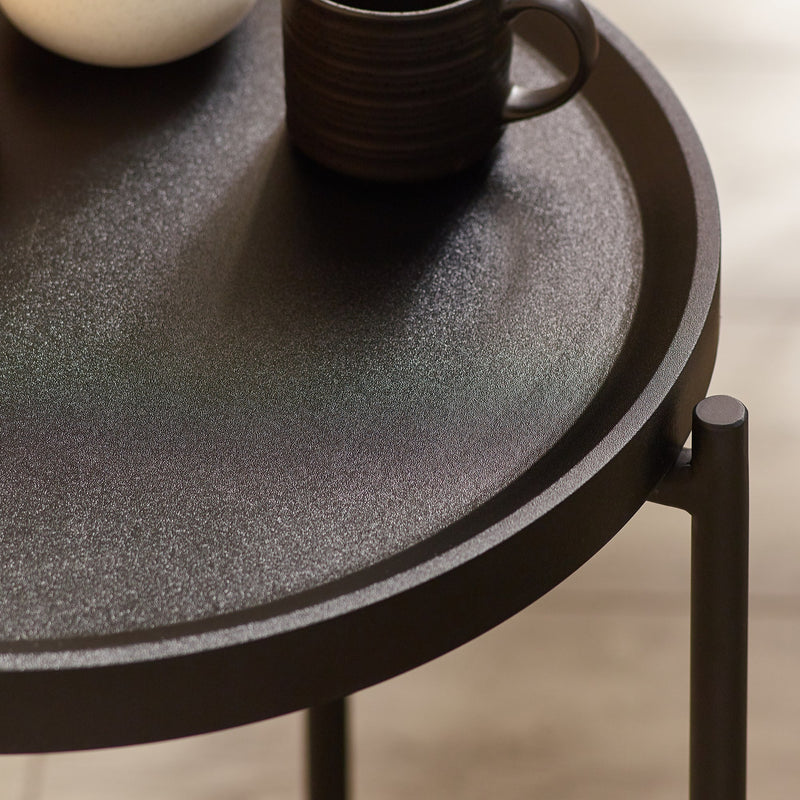 Round black table with a textured surface and a dark ceramic cup on a blurred background