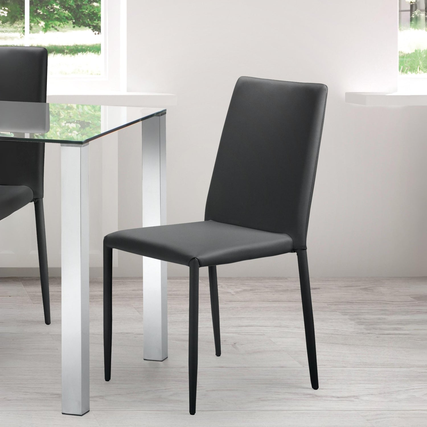 Black chair in front of a glass dining table with white legs in a room with large windows.