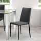 Black chair in front of a glass dining table with white legs in a room with large windows.