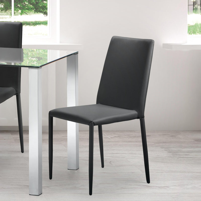 Black chair in front of a glass dining table with white legs in a room with large windows.