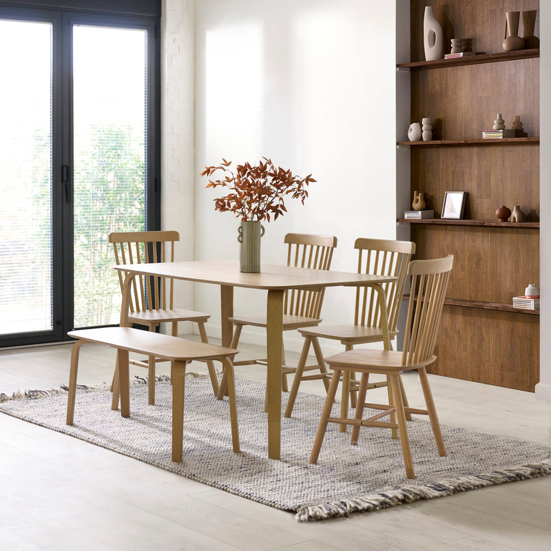 Dining room with wooden table and chairs on a rug, bookshelf in the background