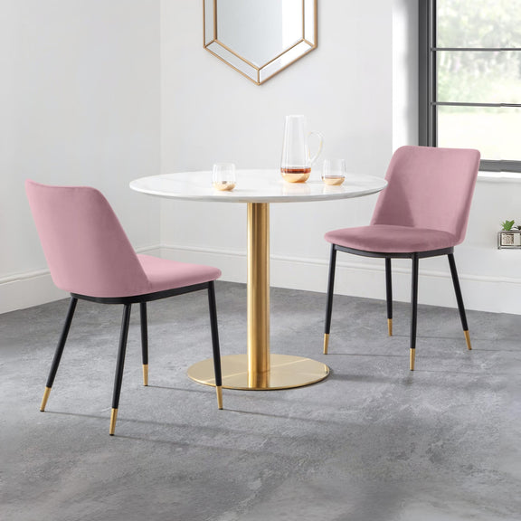 Round dining table with gold base and pink chairs in a room with a mirror and window.