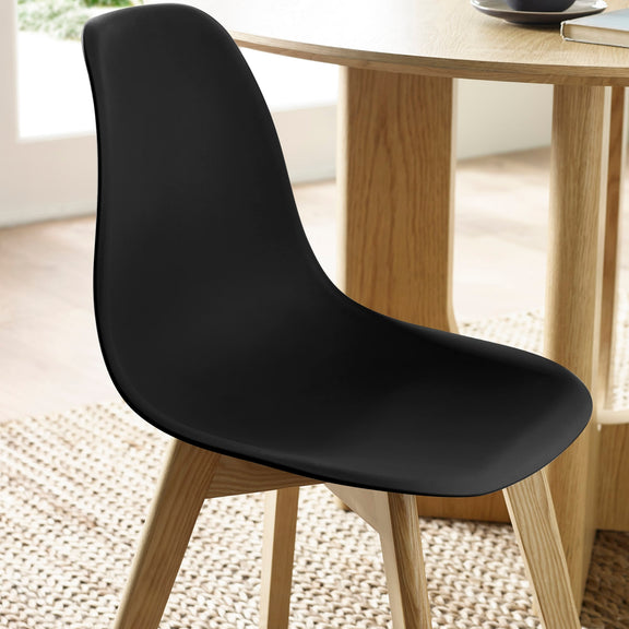 Black chair with wooden legs in a room with a light-colored floor and a table in the background.