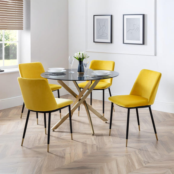 Dining room with a round glass table and yellow chairs on a wooden floor.