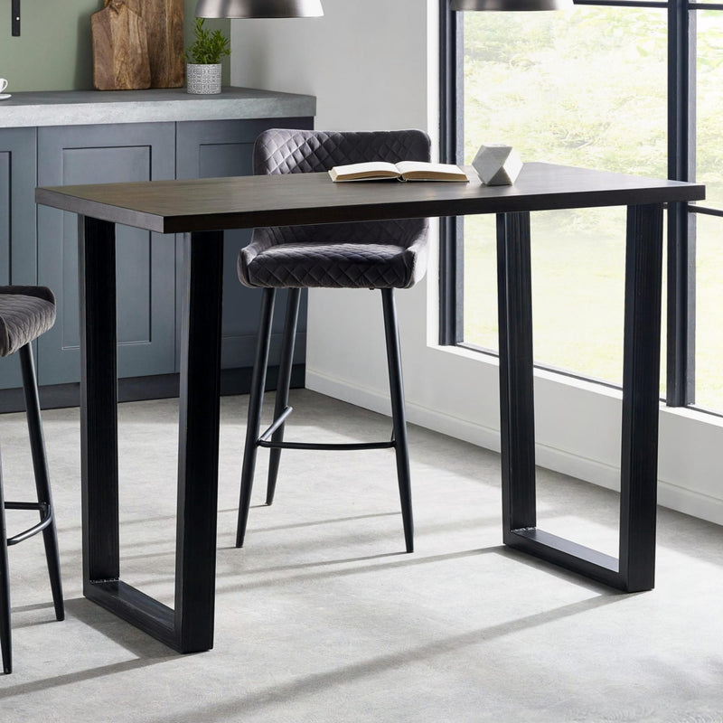Dining table with black metal legs and gray cushioned chairs in a modern kitchen setting.