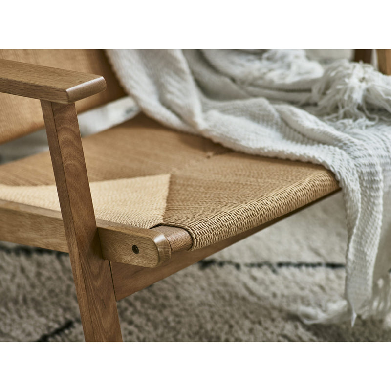 Wooden chair with woven seat and a blanket draped over it on a textured surface.
