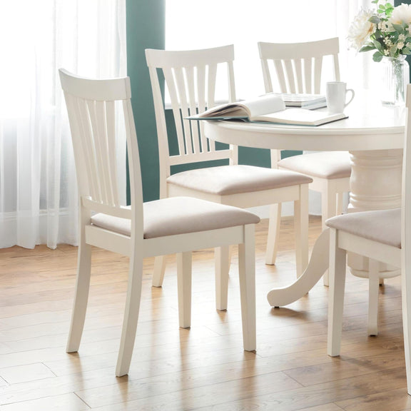 White dining table with four matching chairs in a bright room.