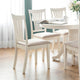 White dining table with four matching chairs in a bright room.