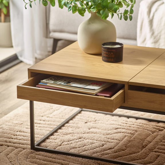 Wooden coffee table with open drawer displaying magazines, a candle, and a vase on top.