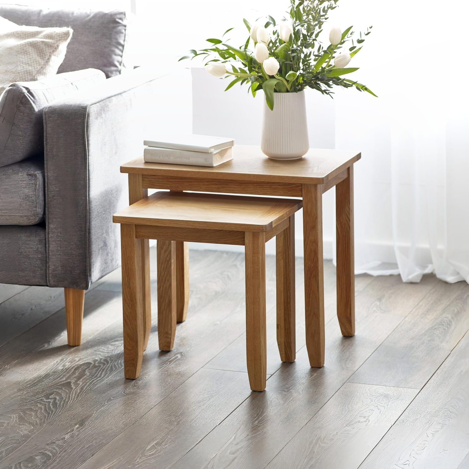 Wooden side table with a vase of flowers next to a gray sofa in a living room.