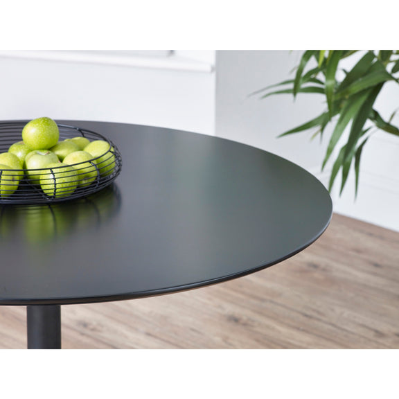 Black round table with a bowl of green apples on a wooden floor.