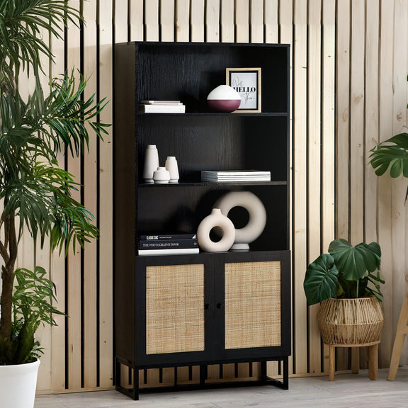 Black bookshelf with wicker doors against a wooden paneled wall with plants around.