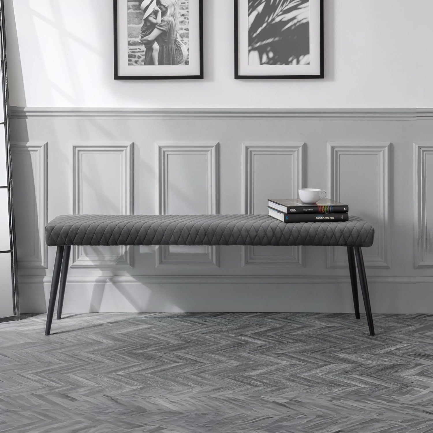 Gray upholstered bench in a room with framed pictures on the wall.