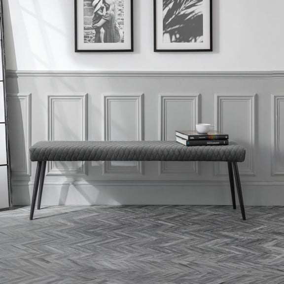 Gray upholstered bench in a room with framed pictures on the wall.
