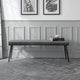 Gray upholstered bench in a room with framed pictures on the wall.